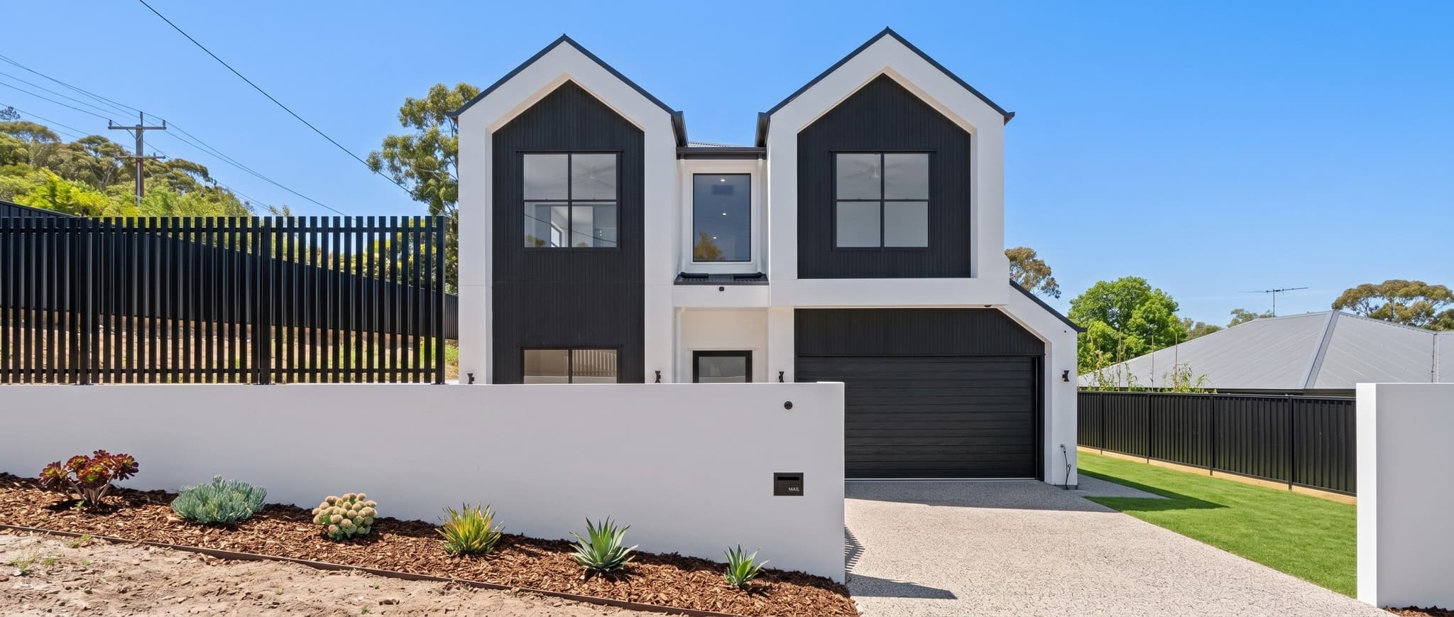 Twin-gabled facade in Carina with black cladding, white render and landscaped front garden.