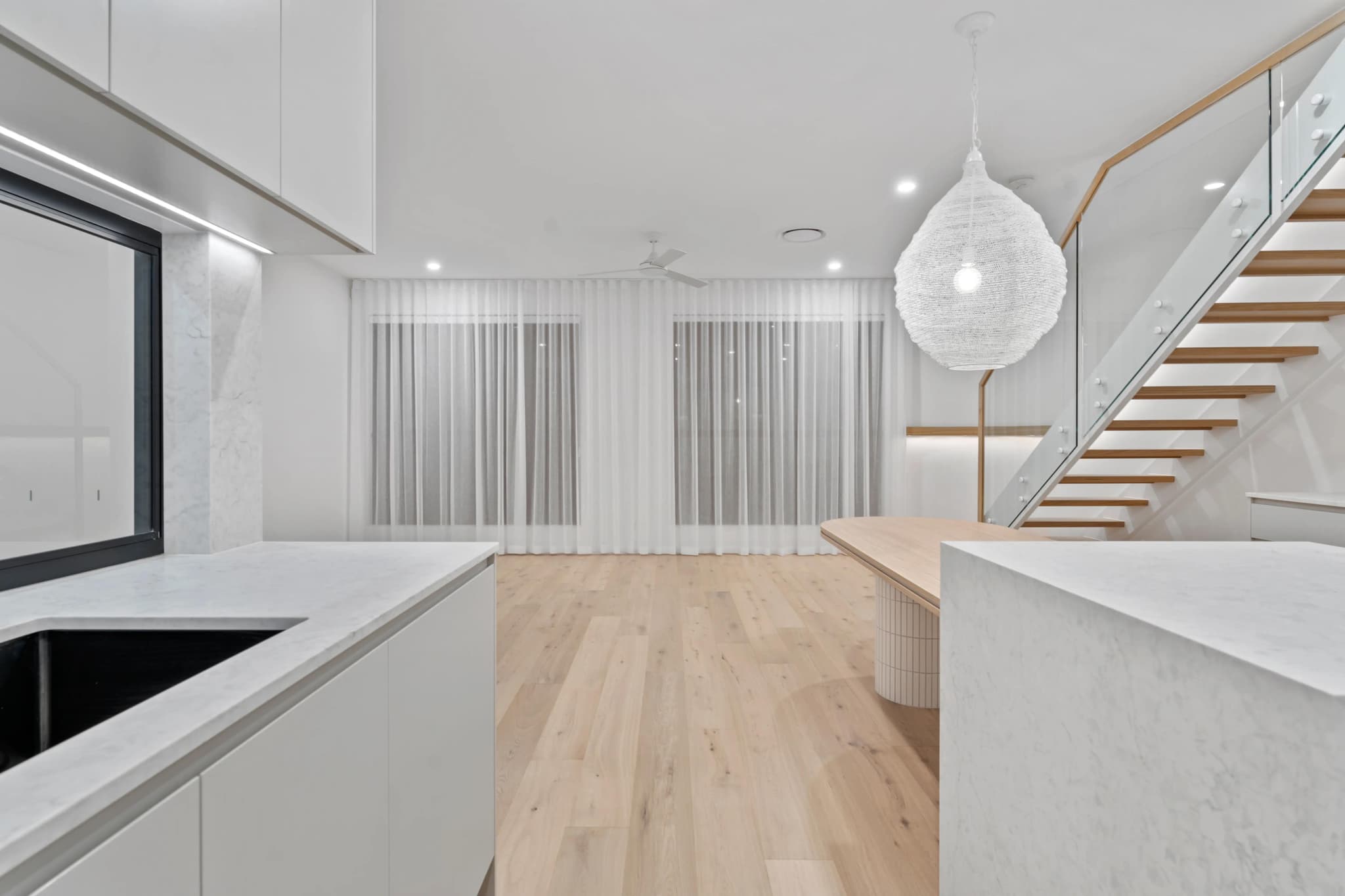 Open living space with stone island, oak dining table and floating timber stair.