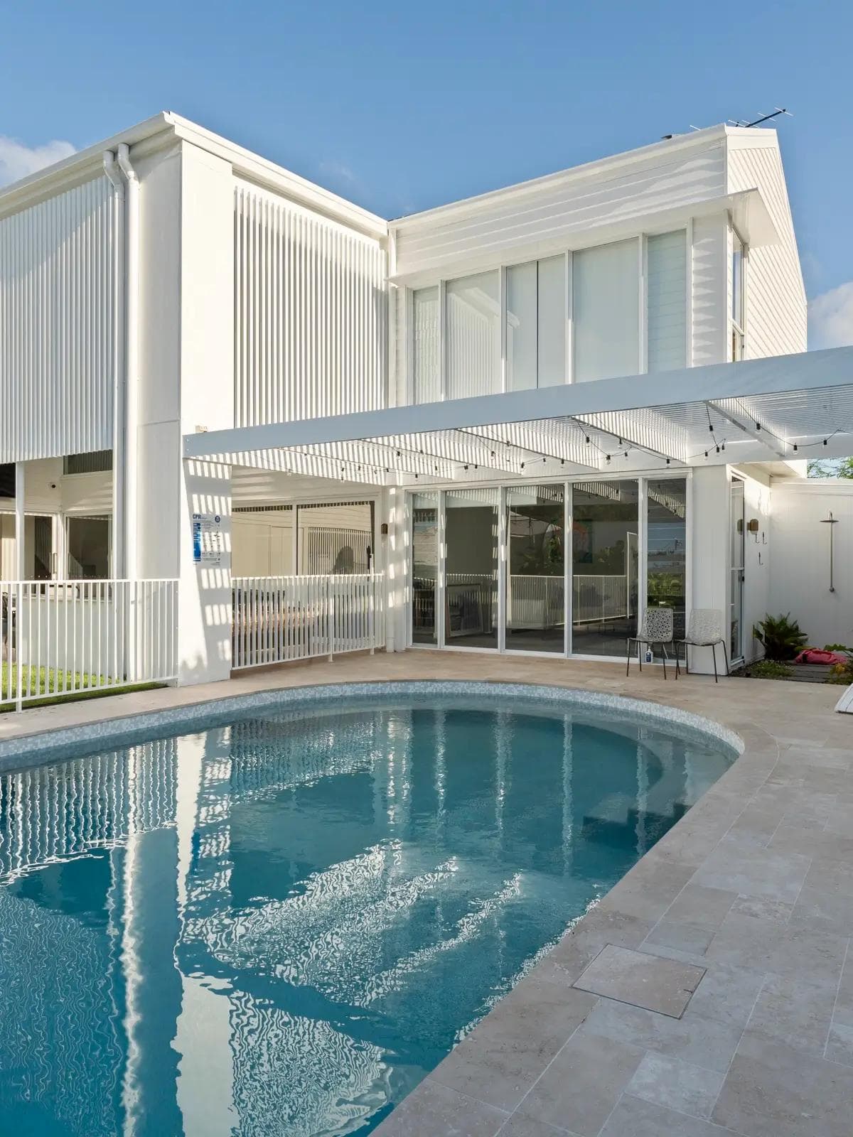 White two-storey home in Seven Hills with battened screens, festoon-lit pergola and curved pool.