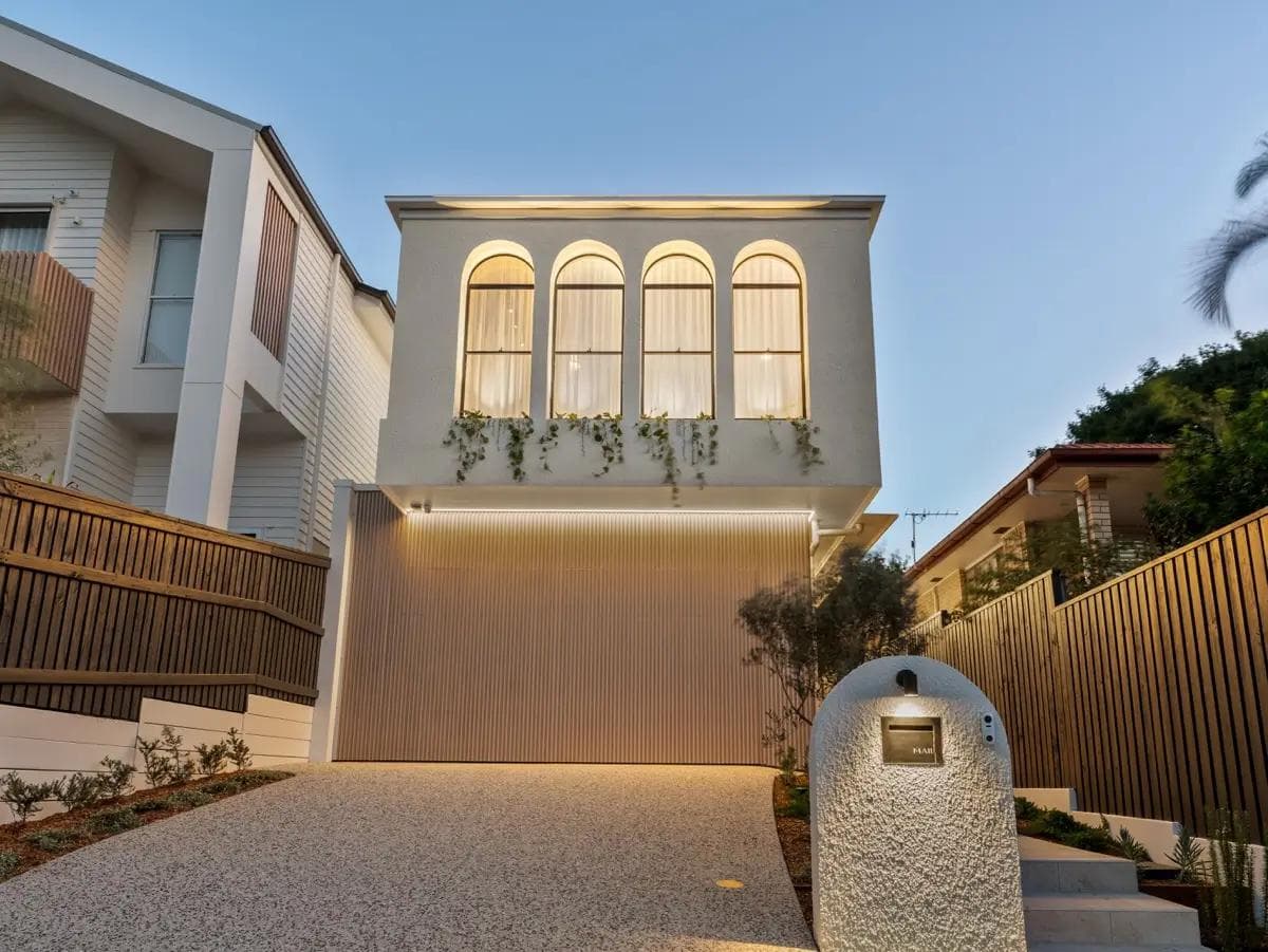 Dusk view of a two-storey Camp Hill home with arched windows, planter box greenery and lit battened garage.