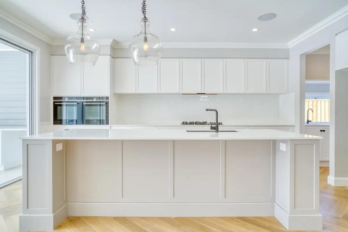 White kitchen with panelled island, glass bell pendants and double wall ovens.