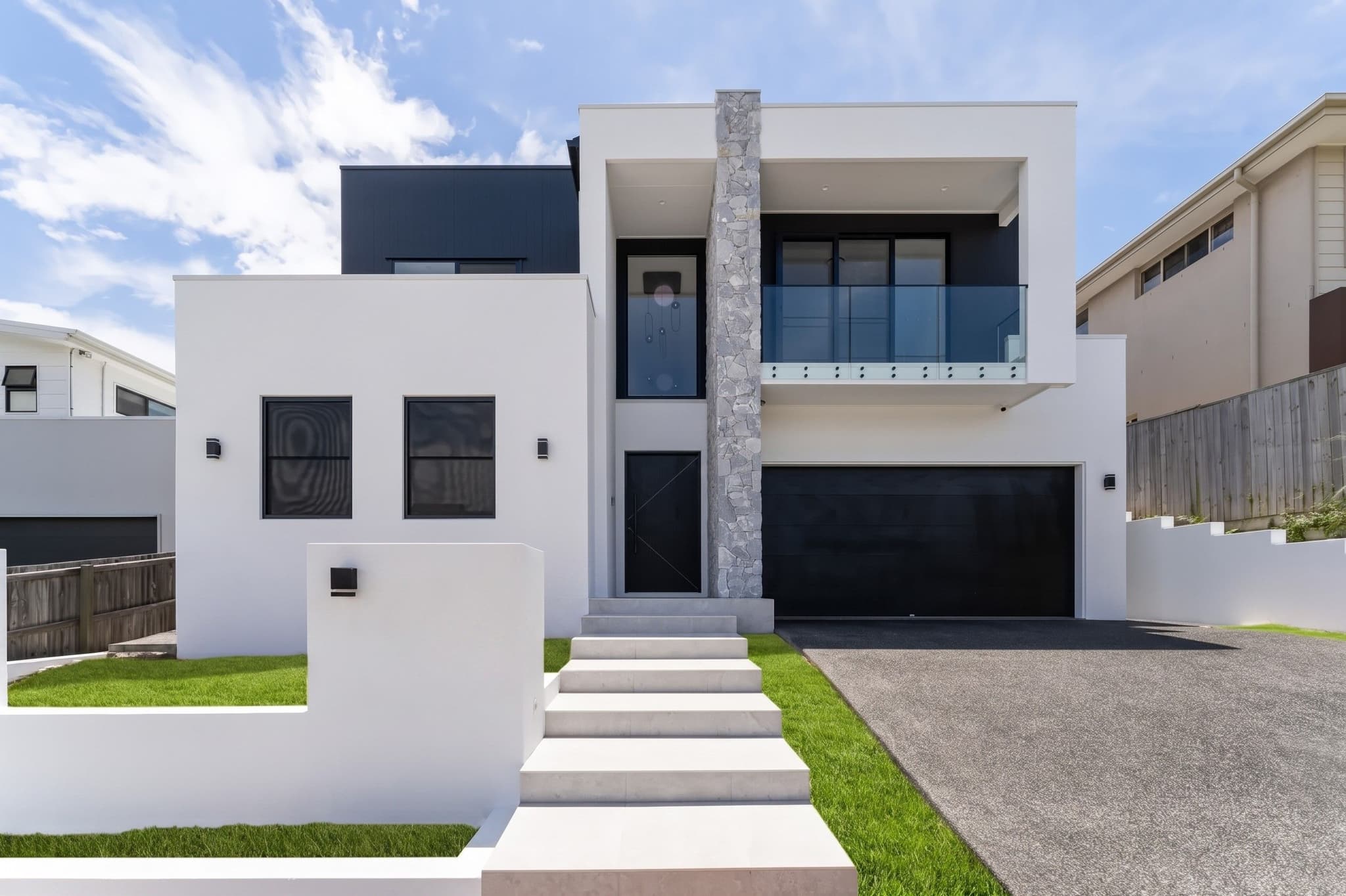 Contemporary two-storey home in Carindale with stone feature blade, glass balcony and dark garage door.