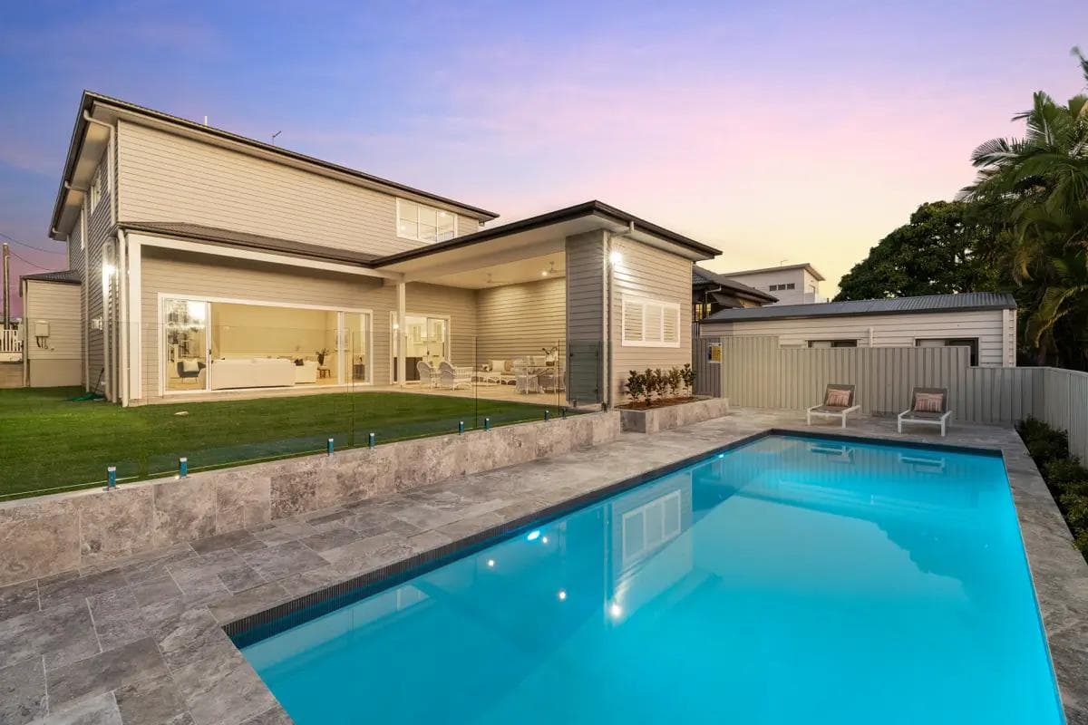 Two-storey Hamptons-style home in Camp Hill with a tiled pool and travertine terrace at dusk.