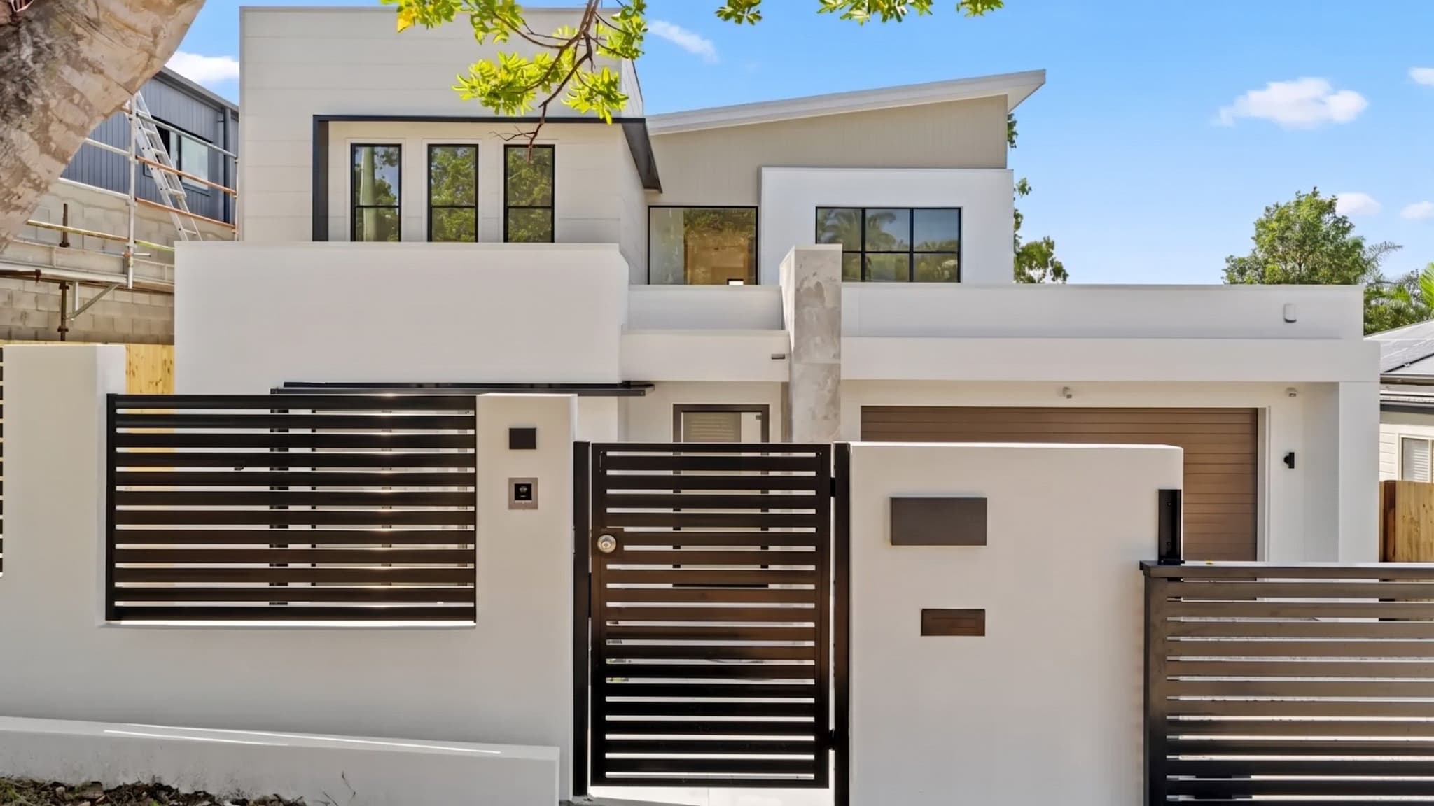 White rendered two-storey home in Camp Hill with skillion roof and black slat fencing and gates.