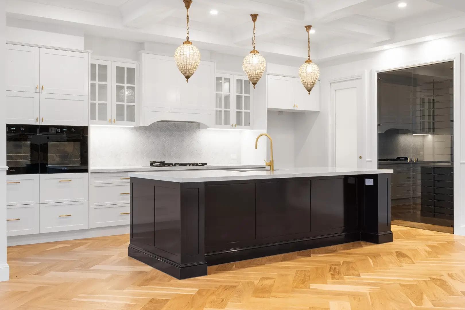 Kitchen with dark shaker island, marble benchtop, brass tapware and beaded pendant lights.