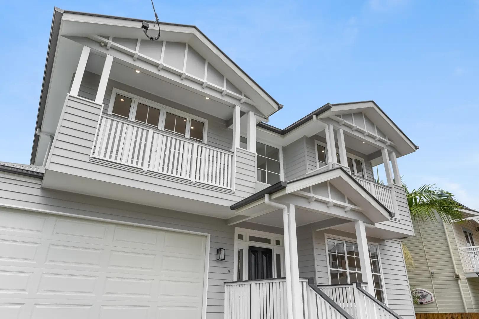 Two-storey Hamptons-style home in Coorparoo with weatherboard cladding, gable roofs and twin balconies.