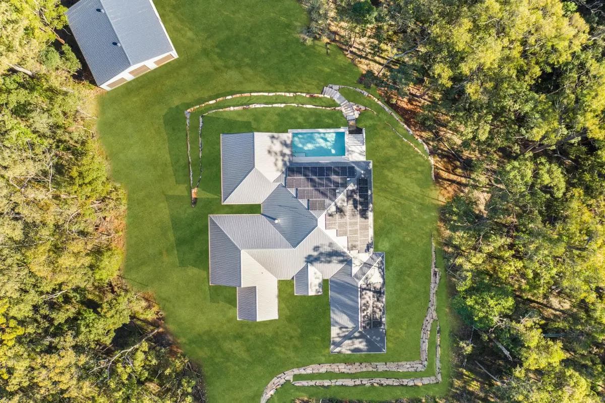 Aerial view of a sprawling custom wide house plan featuring a large roofline, solar panels, and a pool, built on a spacious South East Queensland block.