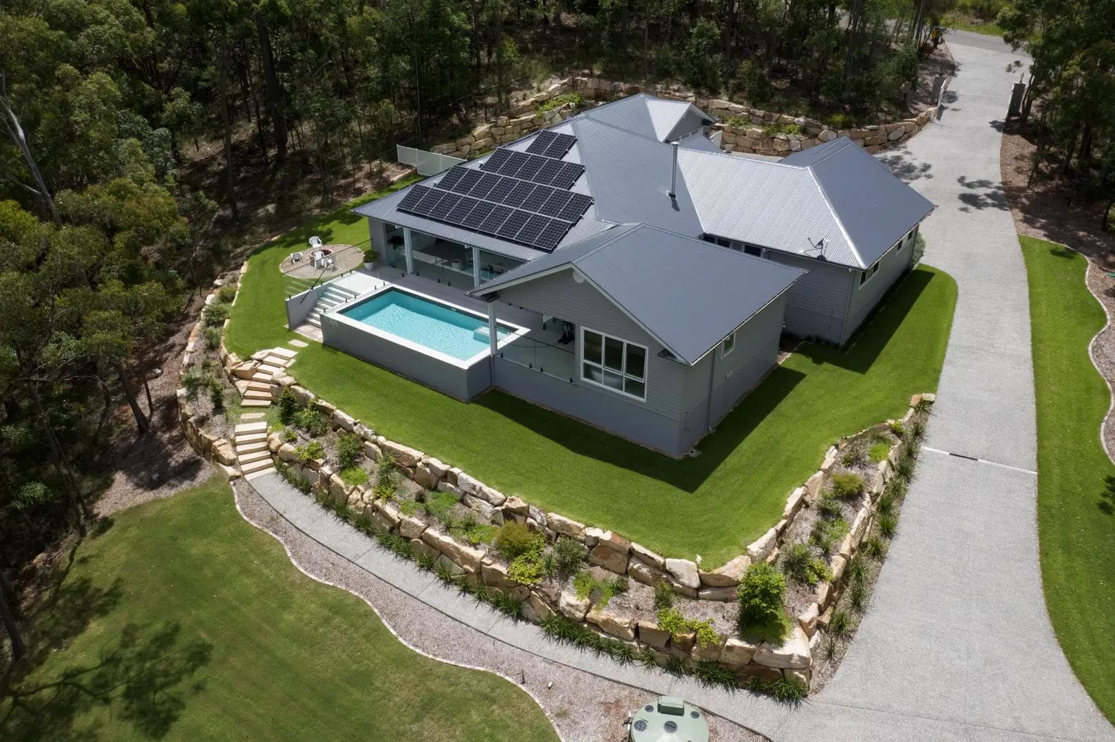 Aerial view of a single-storey acreage home with pool and terraced sandstone gardens in Mackenzie bushland.