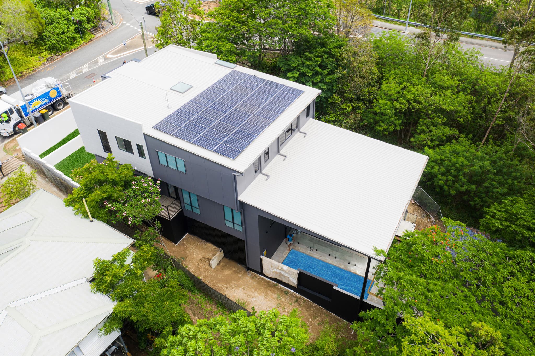 An aerial view of a custom home in Brisbane showcasing a down slope house design with a terraced rear pool and integrated retaining walls.