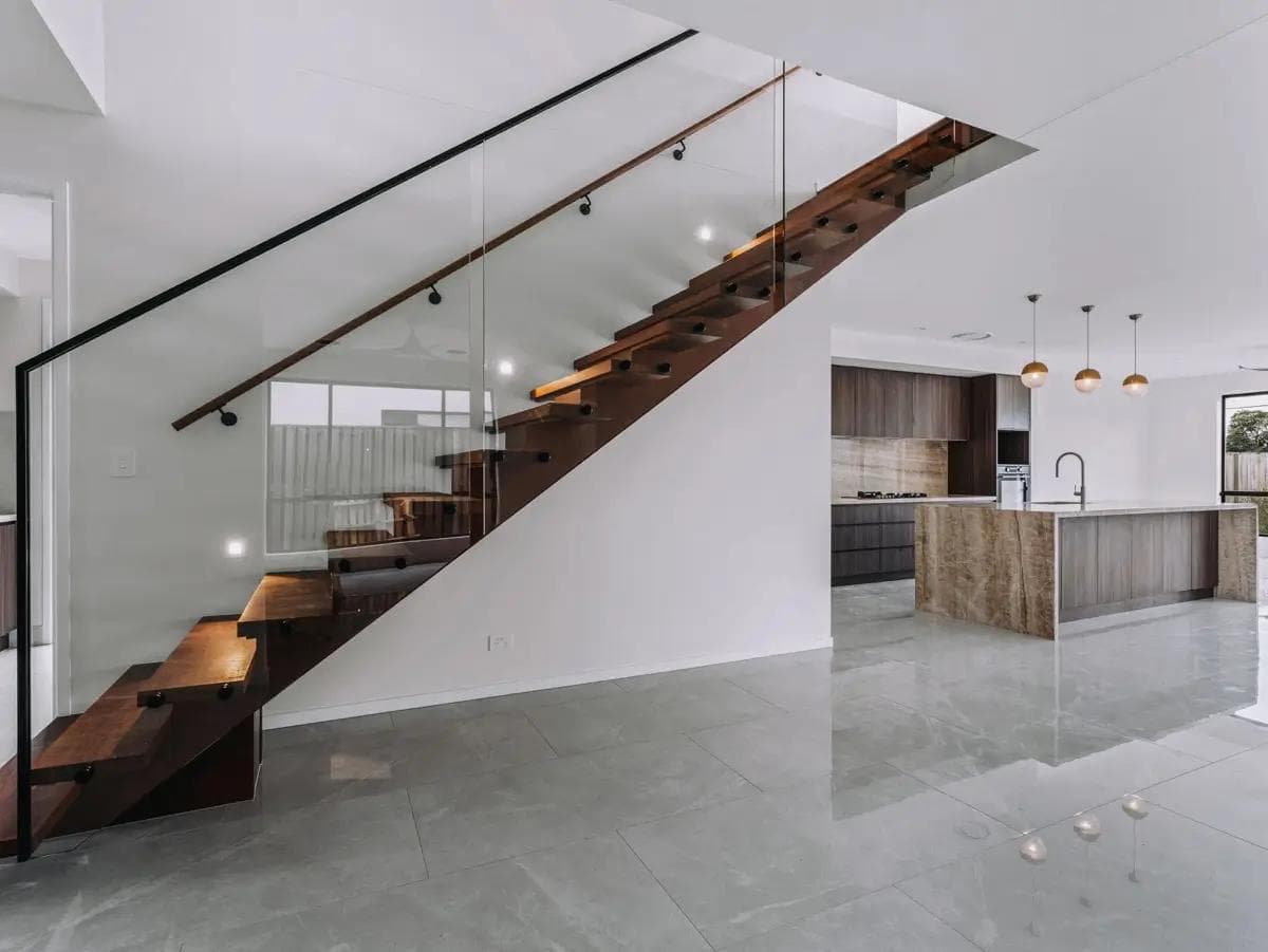Walnut-toned floating stair with glass balustrade beside the stone-clad island kitchen.