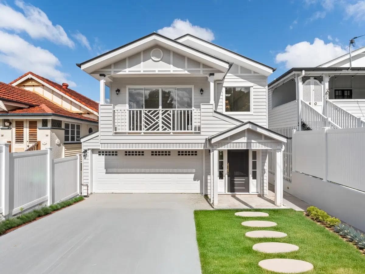 Two-storey Hamptons style home in Greenslopes with white weatherboard cladding, gable roof and balcony.