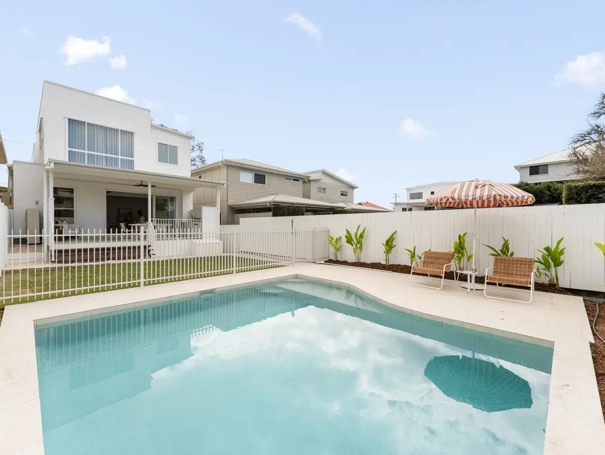 Backyard pool with white fencing, striped umbrella and the covered rear terrace beyond.