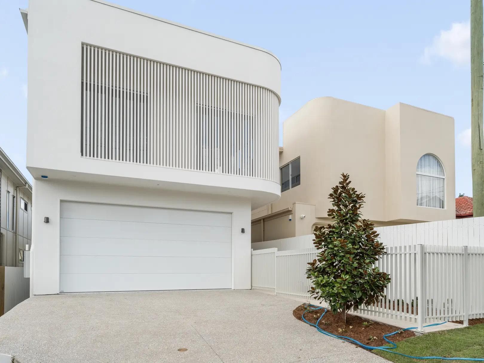 White two-storey home in Morningside with curved corner, vertical battens and stone letterbox pier.