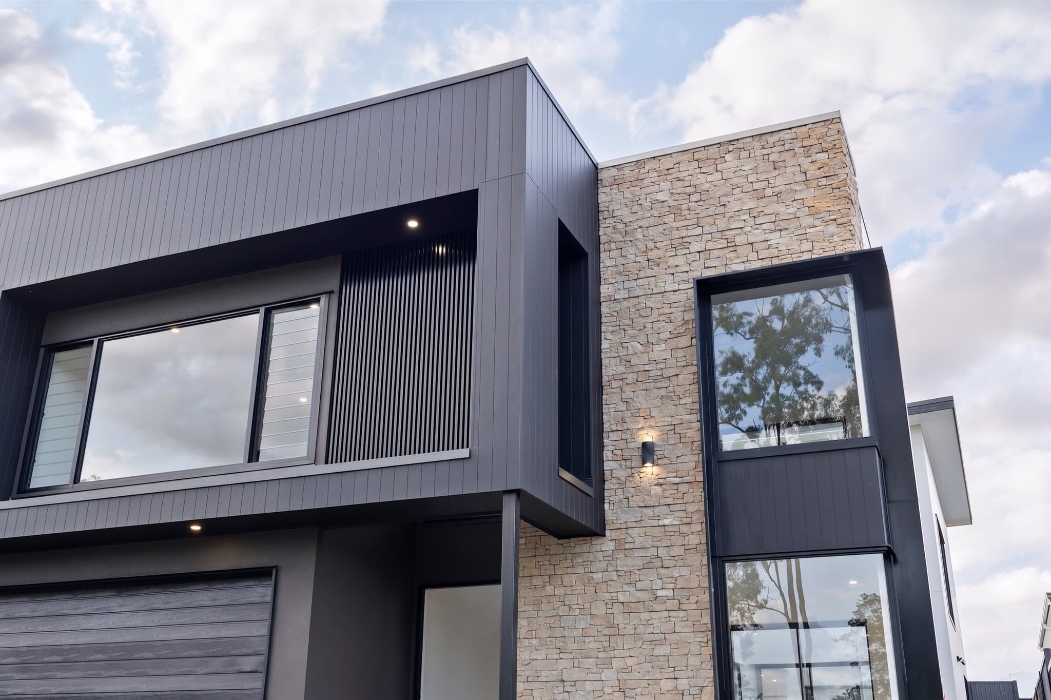 Architectural detail of a contemporary custom home exterior featuring dark charcoal vertical cladding contrasted with a textured natural stone feature wall and black window frames.