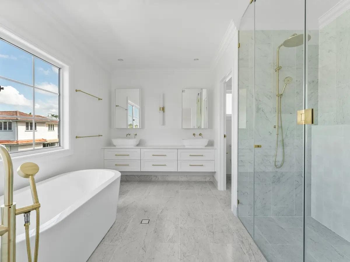 Ensuite with freestanding bath, brass tapware, floating double vanity and marble-tiled shower.