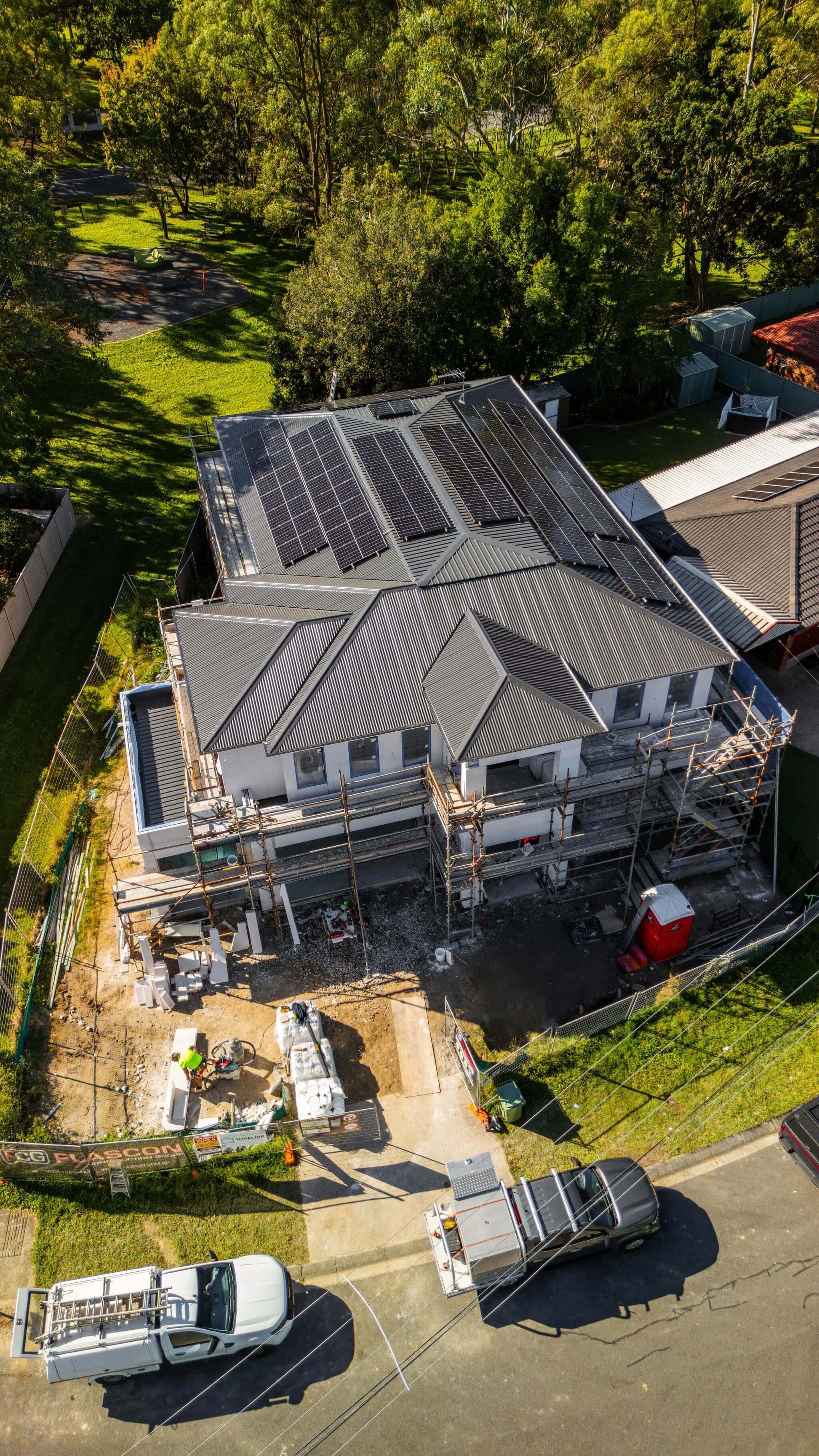 Aerial view of a two-storey custom home under construction in Brisbane, scaffolding in place with roofing and solar panels installed