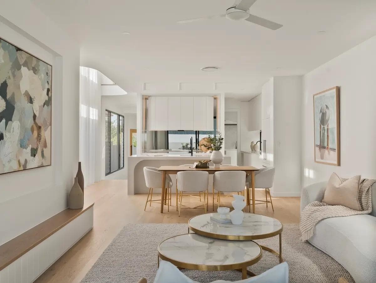 Open-plan living and dining with white kitchen, oak floors and round marble coffee tables.