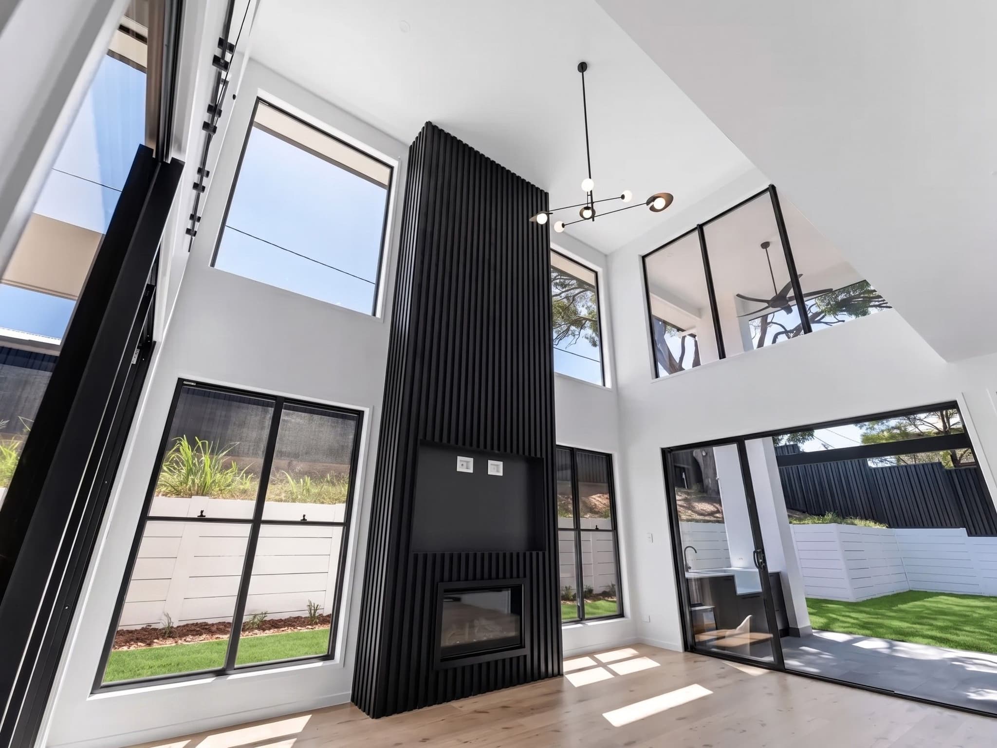 Double-height living space with a black-battened fireplace tower and full-height glazing.