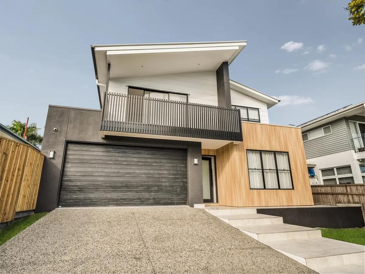 Contemporary two-storey home in Norman Park with timber battens, dark render and balcony.